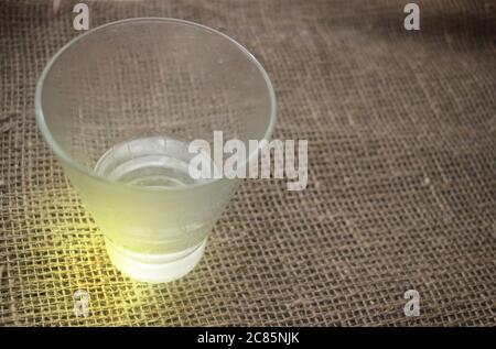 Bicchiere d'acqua o vodka mezzo-pieno in piedi su burlap Foto Stock