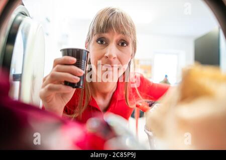 Donna con tazza di caffè guarda in lavatrice Foto Stock