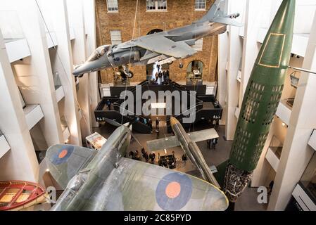 Mostra di aerei del Museo Imperiale della Guerra Londra | LONDRA — Una vista grandangolare dall'alto al Museo Imperiale della Guerra di Londra cattura un aereo da salto Harrier, una Spitfire e un razzo V-2 sospesi sopra i visitatori che si muovono attraverso le scale dell'atrio. L'atrio ridisegnato, completato nel 2014, organizza aerei storici e munizioni per corrispondere alle gallerie cronologiche sottostanti, tracciando la storia militare britannica a partire dalla Prima Guerra Mondiale. Foto Stock