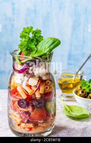 Insalata con pasta, verdure fresche, salumi, olive e formaggio feta in un barattolo - idea di pranzo salutare Foto Stock