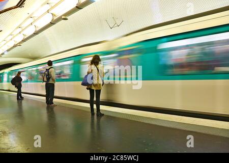 Stazione della metropolitana con treno moderno a Parigi. Un treno sta arrivando mentre tre persone stanno aspettando sulla piattaforma. Foto Stock