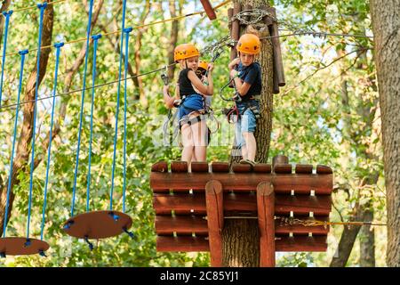 Voronezh, Russia, 23.08.2019 - Bambini in corda alta esperienza parco avventura albero. Bambini su strada corda corso in alberi. Arrampicata avventura corda Park. Foto Stock