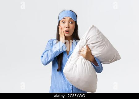 Giovane donna preoccupata e preoccupata in pigiama blu e maschera dormiente, tenendo cuscino e stare gastping ansioso, sentire compassione o pietà per qualcuno ottenuto Foto Stock