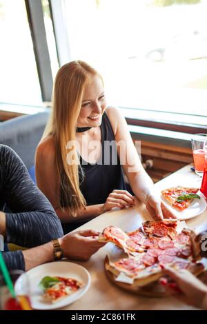 Gruppo di amici che prendono fette di pizza da piatto bianco. Pizza Party, togetherness, concetto di cibo Foto Stock