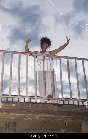 Un attraente modello femminile si pone su una recinzione dal sentiero di un ponte. Foto Stock