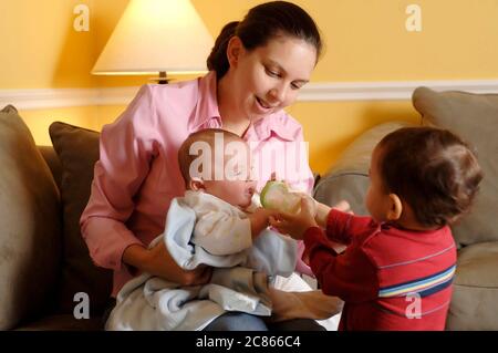 Austin, Texas USA, gennaio 2006: Mamma ispanica, all'inizio degli anni '30, tiene il neonato di tre mesi, mentre il fratello di 22 mesi prova a nutrirsi con un biberon a casa. SIGNOR ©Bob Daemmrich Foto Stock