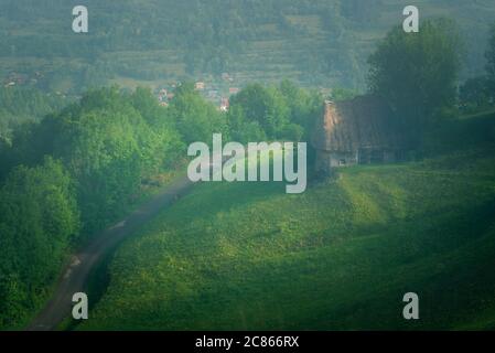 Una bella vecchia casa colonica situata su una collina vista dall'alto vicino a una strada in una giornata di nebbia all'ombra del sole a Dumesti, Salciua de Sus, Alba County, Foto Stock