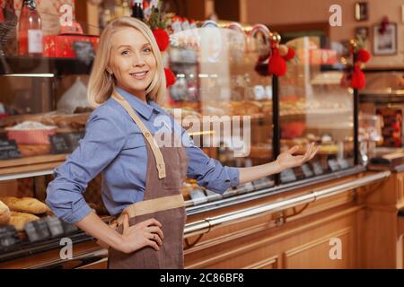 Giovane donna allegra che accoglie giovane al suo negozio di panetteria. Felice donna che lavora nel suo negozio Foto Stock