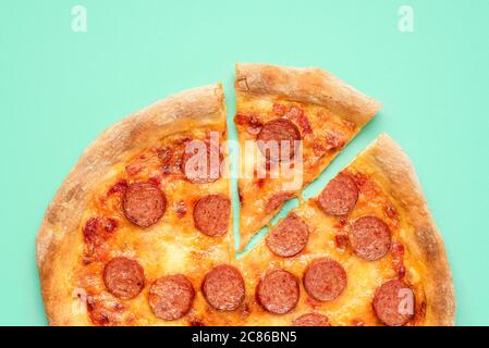 Vista dall'alto con pizza pepperoni fatta in casa su sfondo verde-menta. Fetta di pizza pepperoni, vista dall'alto. Pizza appena sfornata con mozzarella e pomodoro Foto Stock