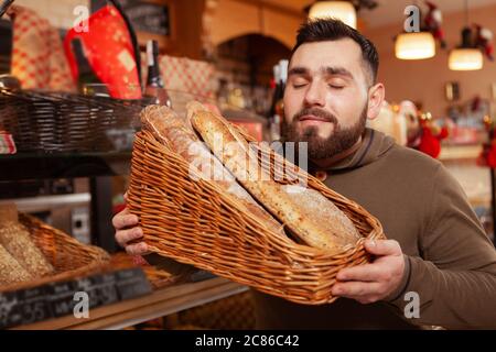 Giovane uomo con bearded che tiene il cestino pieno di pane appena sfornato delizioso, shopping al forno Foto Stock