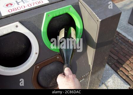 Qualcuno sta mettendo il vetro in un contenitore sotterraneo dei rifiuti nel villaggio di Bergen. Aperture per vetro bianco, verde e marrone. Olanda, gennaio Foto Stock