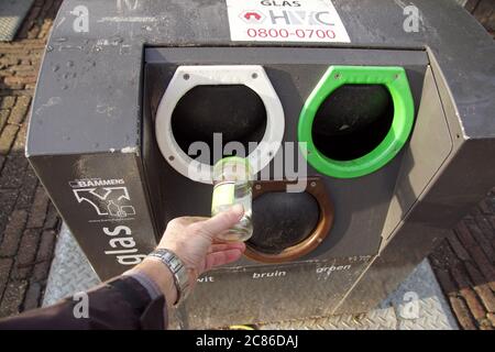 Qualcuno sta mettendo il vetro in un contenitore sotterraneo dei rifiuti nel villaggio di Bergen. Aperture per vetro bianco, verde e marrone. Olanda, gennaio Foto Stock