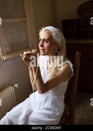 Donna matura che prega con un rosario Foto Stock