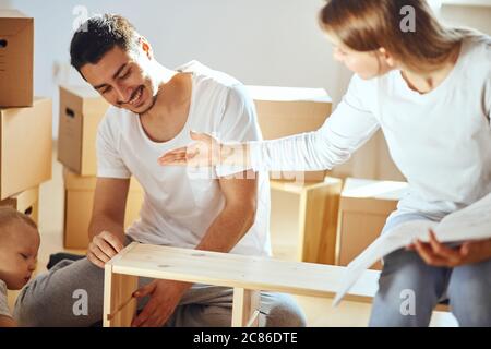 Coppia legge le istruzioni per l'assemblaggio di mobili in una nuova casa con scatole mobili sullo sfondo Foto Stock