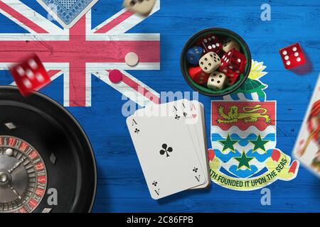 Tema del casinò delle Isole Cayman. Assi nel gioco del poker, carte e chip sul tavolo rosso con sfondo bandiera nazionale. Gioco d'azzardo e scommesse. Foto Stock