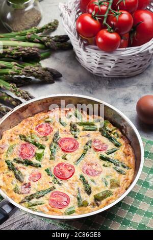 Frittata fatta di uova, asparagi e pomodori ciliegini su una padella. Cucina italiana Foto Stock