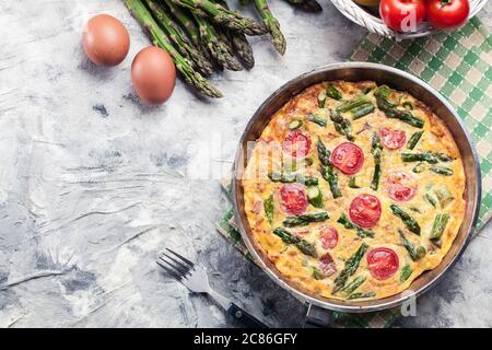 Frittata fatta di uova, asparagi e pomodori ciliegini su una padella. Cucina italiana Foto Stock