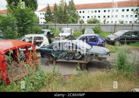 Scrazioso pieno di carcasse di auto in una città provinciale dell'Europa orientale circondata da una recinzione di ferro corrugato. Foto Stock