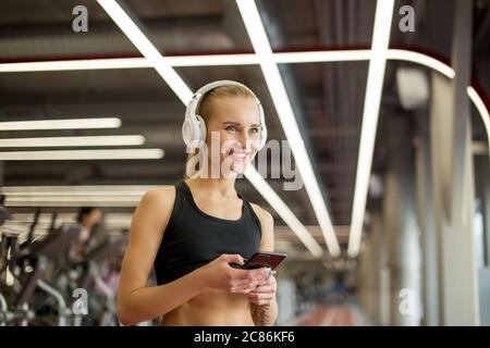 Bella sportiva caucasica che ascolta la musica sul suo cellulare in palestra Foto Stock