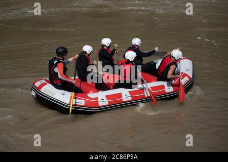 I membri della squadra di rafting e l'istruttore che si candida in barca lungo il fiume torbido durante una giornata estiva. Practicing sport acquatici può essere buono per il vostro streng Foto Stock