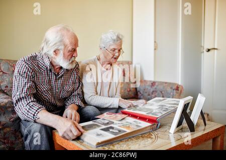 Coppia europea anziana di pensionati seduti in un accogliente soggiorno guardando le foto del loro matrimonio e della nascita del primo bambino e ricordando felice Foto Stock