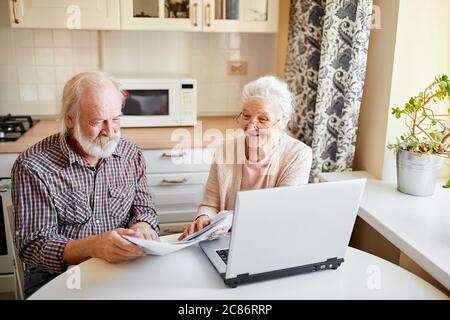 Felice giovane coppia allegra ottenere buone notizie su e-mail circa il loro deposito bancario, seduto in una cucina accogliente con il computer portatile e controllare il loro interesse annuale Foto Stock