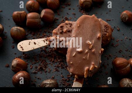 Dessert surgelati e snack estivi con primo piano su due deliziosi gelati al cioccolato e alle nocciole circondati da nocciole sparse, cacao Foto Stock