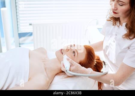 Hardware cosmetologia. Chiudere l immagine della donna attraente con i capelli di zenzero fresco e pelle freckled ricezione rf procedura di sollevamento in un centro di bellezza. Foto Stock