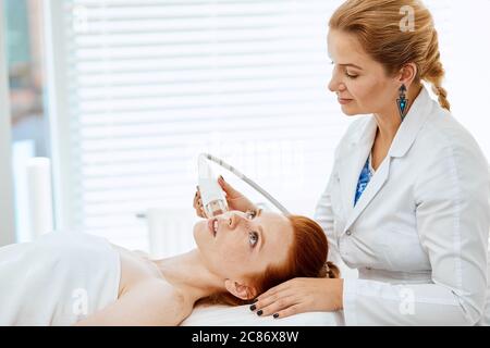 Cosmetologo professionista che fa trattamento viso anti-rughe. Concetto di cura della pelle e correzione della consistenza della pelle. Paziente femminile che riceve frequenza radio Foto Stock