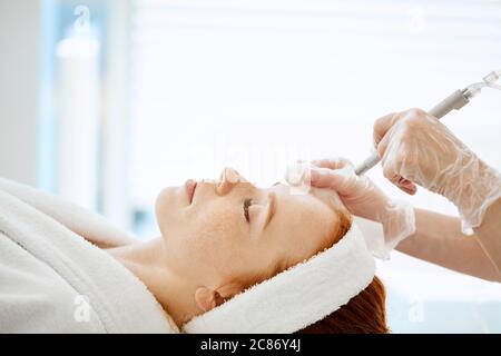 Donna caucasica che ottiene la procedura di peeling del viso in una clinica di bellezza, primo piano. Trattamento rigenerante con gas viso liquido. Idropulente per la pelle ad aria Foto Stock