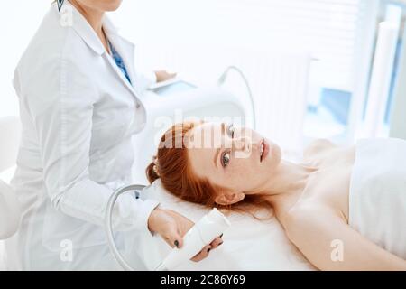 Hardware cosmetologia. Chiudere l immagine della donna attraente con i capelli di zenzero fresco e pelle freckled ricezione rf procedura di sollevamento in un centro di bellezza. Foto Stock