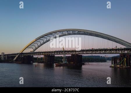 Costruzione di un nuovo ponte ad arco sul fiume Dnipro (Dnieper), Kiev, Ucraina. Vista al tramonto della grande infrastruttura sull'acqua Foto Stock