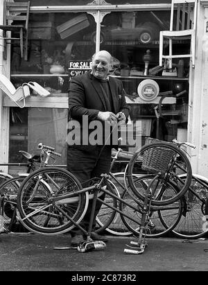 AJAXNETPHOTO. 26 GENNAIO 1975. SOUTHSEA, PORTSMOUTH, INGHILTERRA. - RIPARAZIONI BICI - IL PROPRIETARIO DI SKIPPERS BICYCLE NEGOZIO FUORI SEDE CON IL SUO CANE IN STRADA CASTELLO. PHOTO:JONATHAN EASTLAND/AJAX REF:7504 202206 27 Foto Stock