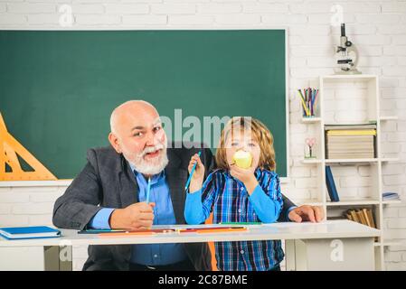 Insegnamento individuale. Ritratto di un insegnante senior e di un ragazzino seduto alla scrivania in classe. Insegnante di uomo maturo e allievo su sfondo di balkboard Foto Stock