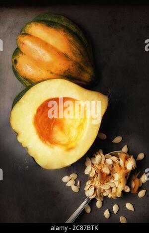 Immagine piatta di una zucca di Acorn tagliata a metà su una lamiera da forno con un cucchiaio e semi scopati con luce laterale calda. Foto Stock