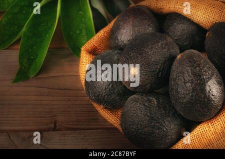 Ancora vita di avocado Hass in un sacco di scasso su uno sfondo di legno con foglie e calda luce laterale. Foto Stock