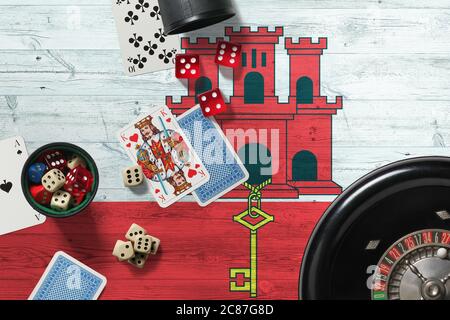 Tema del casinò di Gibilterra. Assi nel gioco del poker, carte e chip sul tavolo rosso con bandiera nazionale di legno sfondo. Gioco d'azzardo e scommesse. Foto Stock