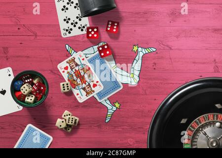 Tema del casinò dell'isola di Man. Assi nel gioco del poker, carte e chip sul tavolo rosso con bandiera nazionale di legno sfondo. Gioco d'azzardo e scommesse. Foto Stock