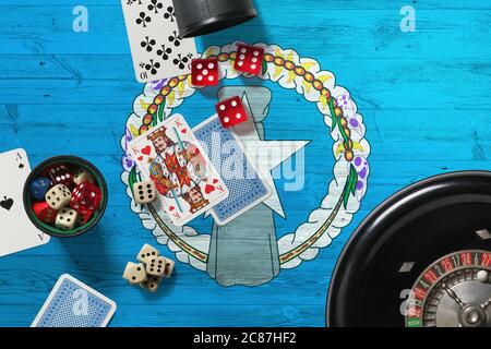 Tema del casinò delle Isole Marianne Settentrionali. Assi nel gioco del poker, carte e chip sul tavolo rosso con bandiera nazionale di legno sfondo. Gioco d'azzardo e scommesse. Foto Stock