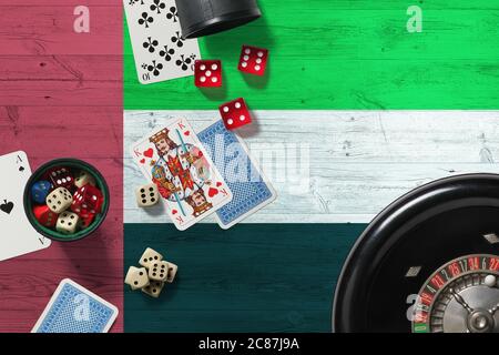 Tema del casinò degli Emirati Arabi Uniti. Assi nel gioco del poker, carte e chip sul tavolo rosso con bandiera nazionale di legno sfondo. Gioco d'azzardo e scommesse. Foto Stock