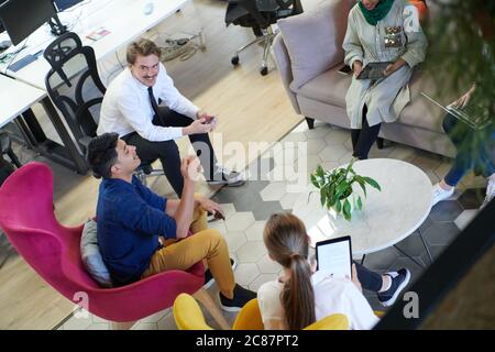 Team aziendale multietnico che ha un brainstorming nell'area relax degli interni moderni dell'ufficio che lavorano su computer laptop e tablet Foto Stock