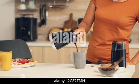 Donna che versa caffè caldo in tazza al mattino dalla pentola. Casalinga a casa, preparare caffè macinato fresco in cucina per colazione, bere, macinare caffè espresso prima di andare al lavoro Foto Stock