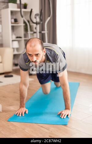 Mettere l'uomo nel suo appartamento facendo scalatori di montagna esercizio su tappeto yoga durante la pandemia globale. Foto Stock