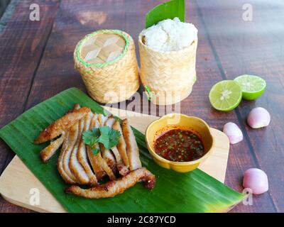 Collo di maiale alla griglia con salsa piccante servita su vassoio di legno e riso appiccicoso servito in contenitore di stile orientale - molto famoso antipasto di cibo tailandese ( KOR MOO Foto Stock