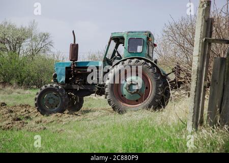 Un vecchio trattore blu arata un campo e coltiva il terreno. Agricoltura. Foto Stock