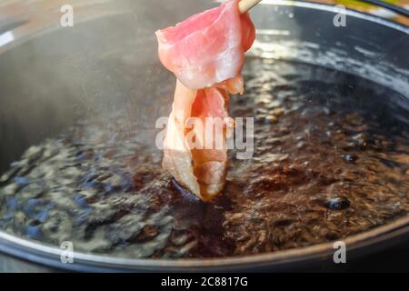 Con i bastoncini, raccogliere il maiale tagliato a fette crudo sulla zuppa calda con fumo per l'immersione e la caduta di Shabu Shabu o Sukiyaki. Il cibo popolare è cucinato p Foto Stock