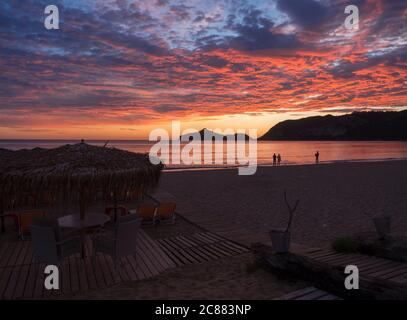 Belle nuvole blu rosa arancio dopo il tramonto sulla spiaggia di Aghios Georgios Pagon sull'isola di Corfù, Grecia con ombrelloni lettini e sillhoutes vuoti Foto Stock