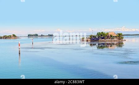 isole e canali navigabili nella laguna blu di grado con le alpi Carniche innevate sullo sfondo, Italia Foto Stock