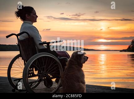 Donna in sedia a rotelle al tramonto con cane Foto Stock