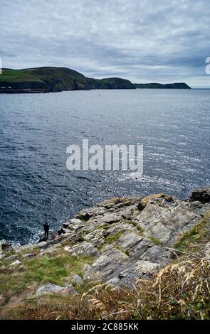 Lone pescatore su rocce sul lato della baia di Port Erin, Isola di Man Foto Stock